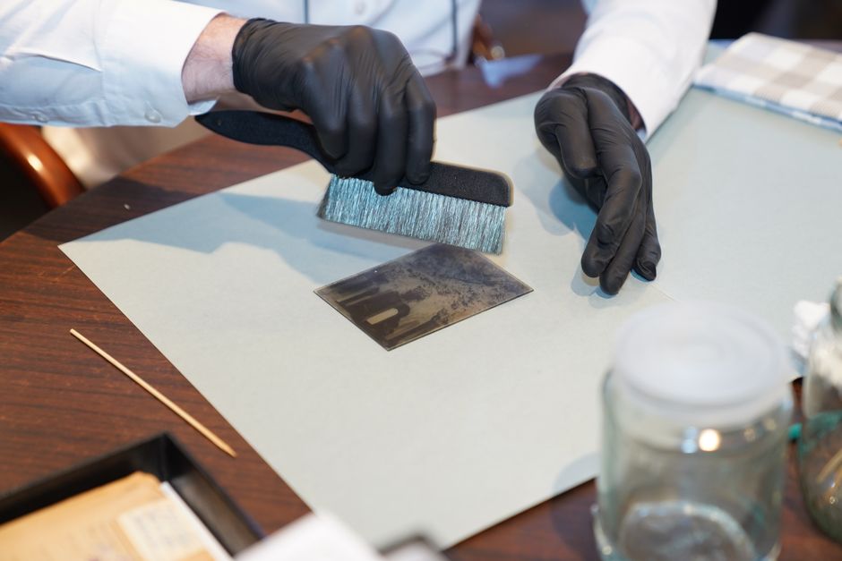A person's hand is seen holding a white cleaning sponge while carefully restoring the delicate fabric of an upholstered piece of furniture, likely a sofa, in a well-lit room with soft blue tones. The fabric appears smooth and clean, with visible surface details indicating gentle surface cleaning. In the background, a portion of the fabric's cushioning is visible, and the environment suggests a focus on meticulous domestic cleaning care, aligning with the importance of choosing a certified cleaner for delicate heritage fabric restoration, as highlighted by One-Off Cleaning.